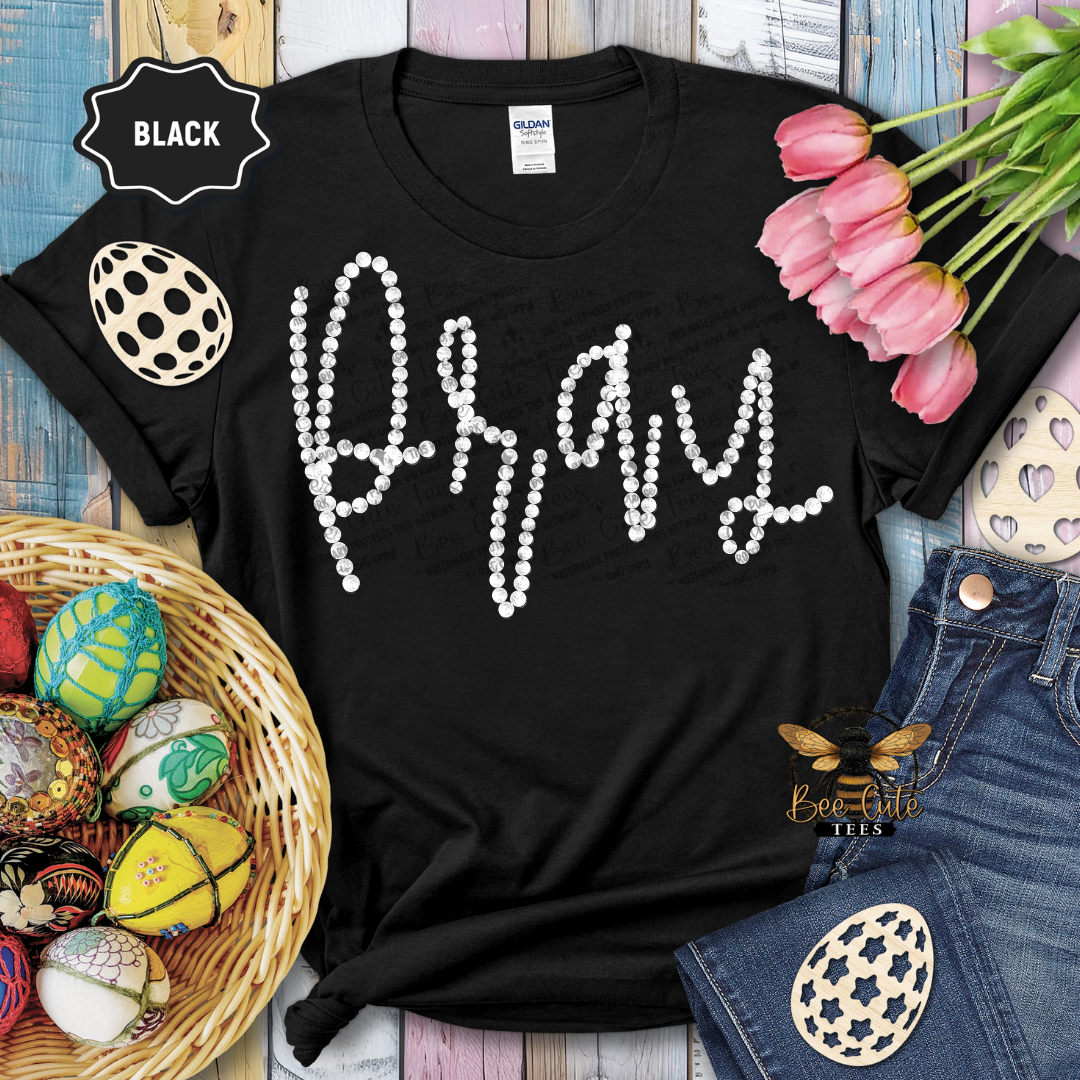 Black t-shirt with 'Happy' in pearls, surrounded by Easter decorations on a wooden surface.