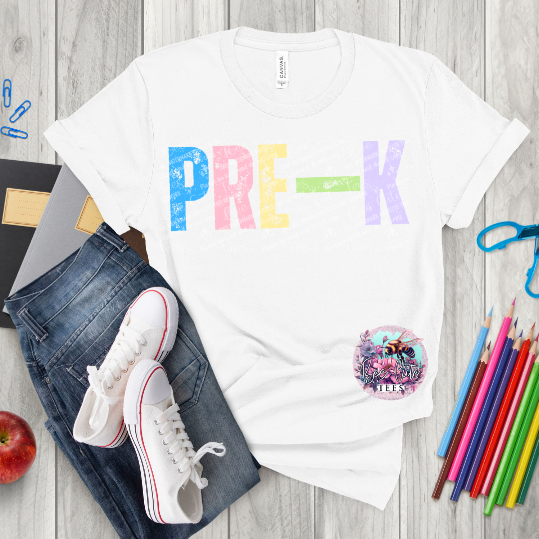 White t-shirt with 'PRE-K' in colorful letters, jeans, sneakers, and school supplies on a wooden surface.
