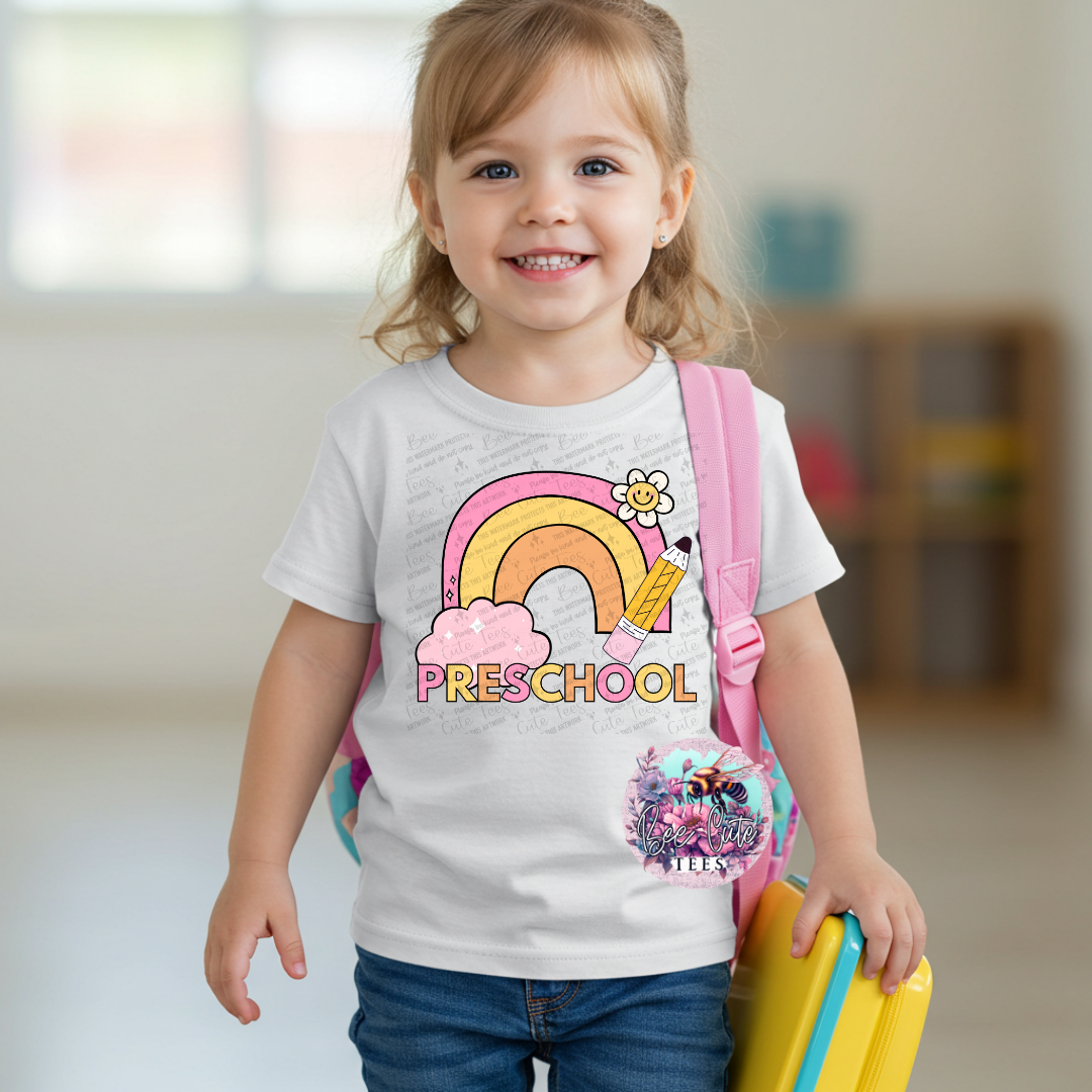 Child wearing a 'PRESCHOOL' t-shirt with a rainbow design, holding a yellow toy.