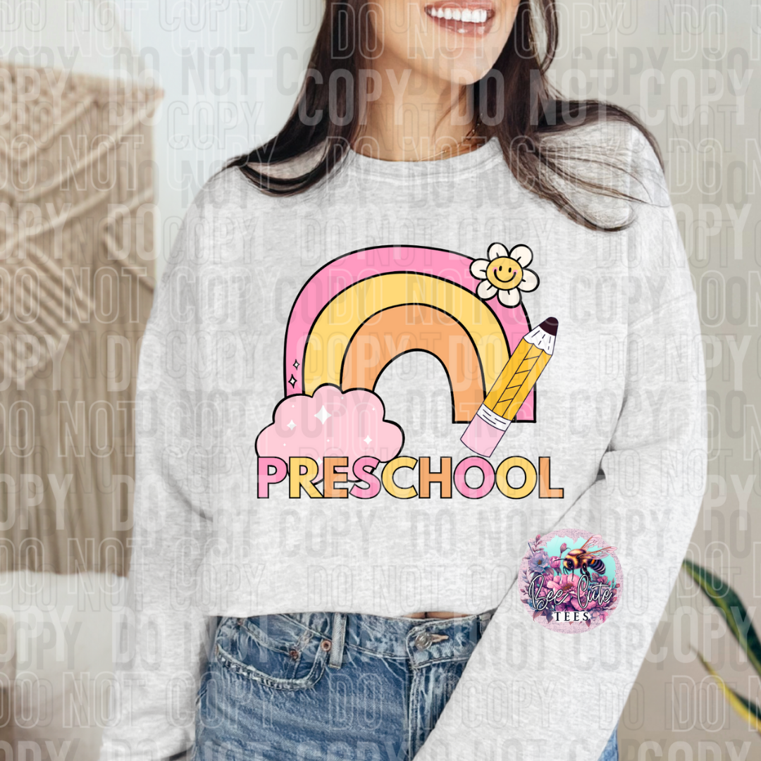 Person wearing a white sweatshirt with a colorful 'Preschool' design featuring a rainbow, pencil, and flower.