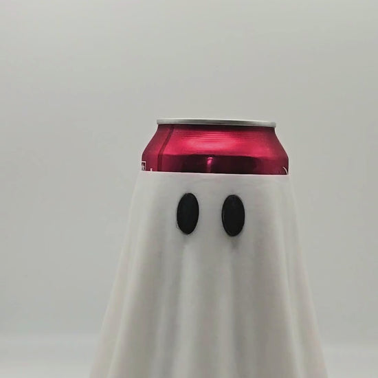a video representation on how to use a nail saver.  A canned soda inside of a ghost can holder and a person using a ghost shaped nail saver to open the soda can.