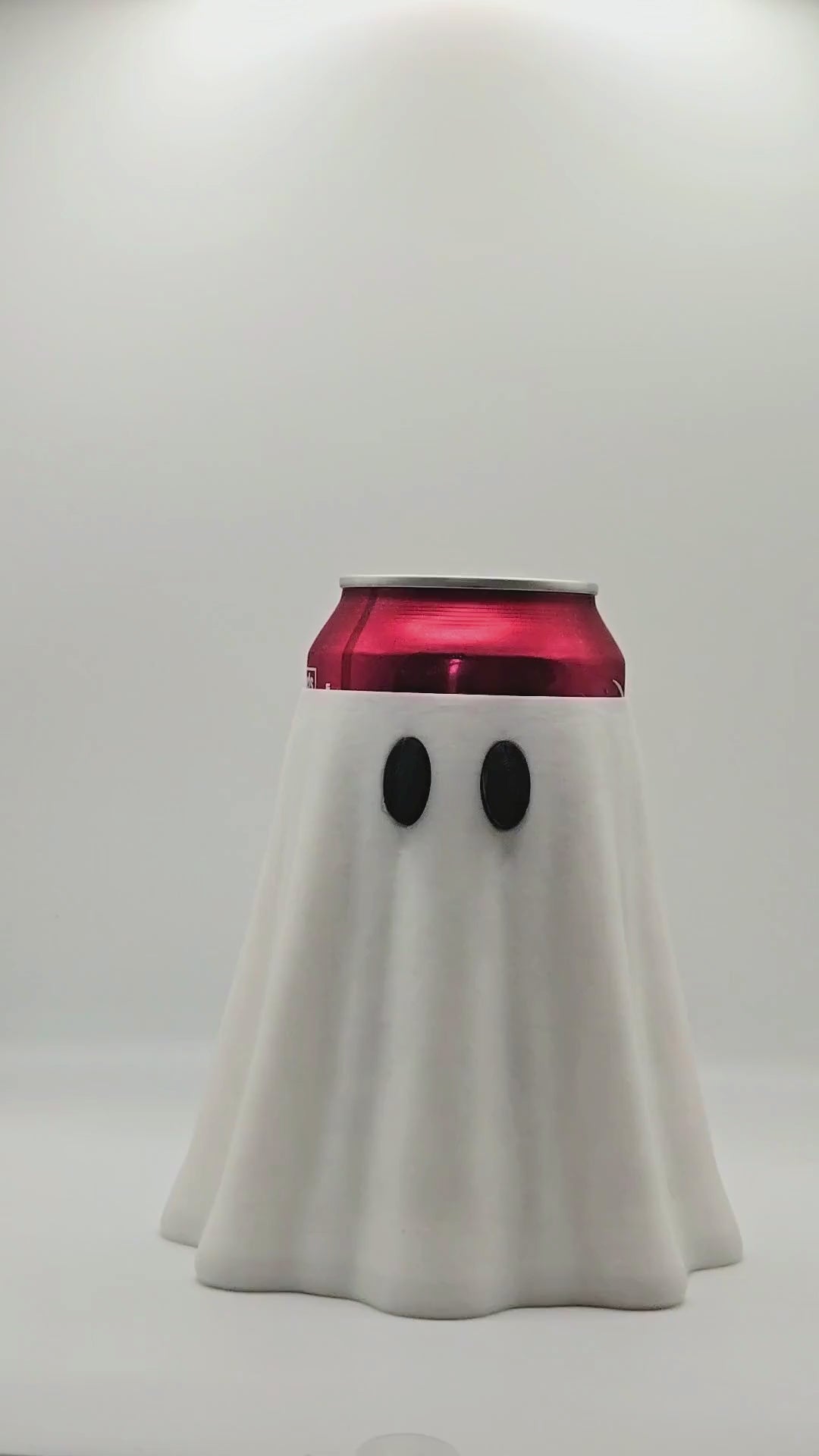 a video representation on how to use a nail saver.  A canned soda inside of a ghost can holder and a person using a ghost shaped nail saver to open the soda can.