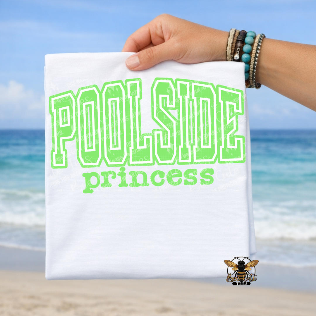 Hand holding a t-shirt with 'Poolside princess' text against a beach background