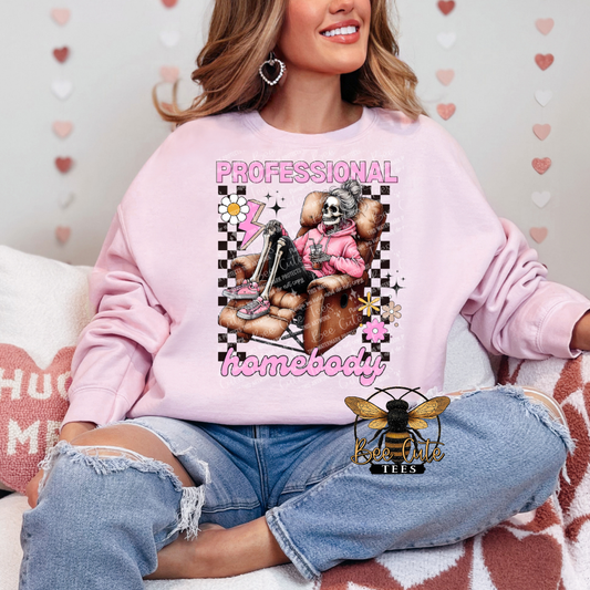 Person wearing a pink sweatshirt with a graphic design and text, sitting on a couch.