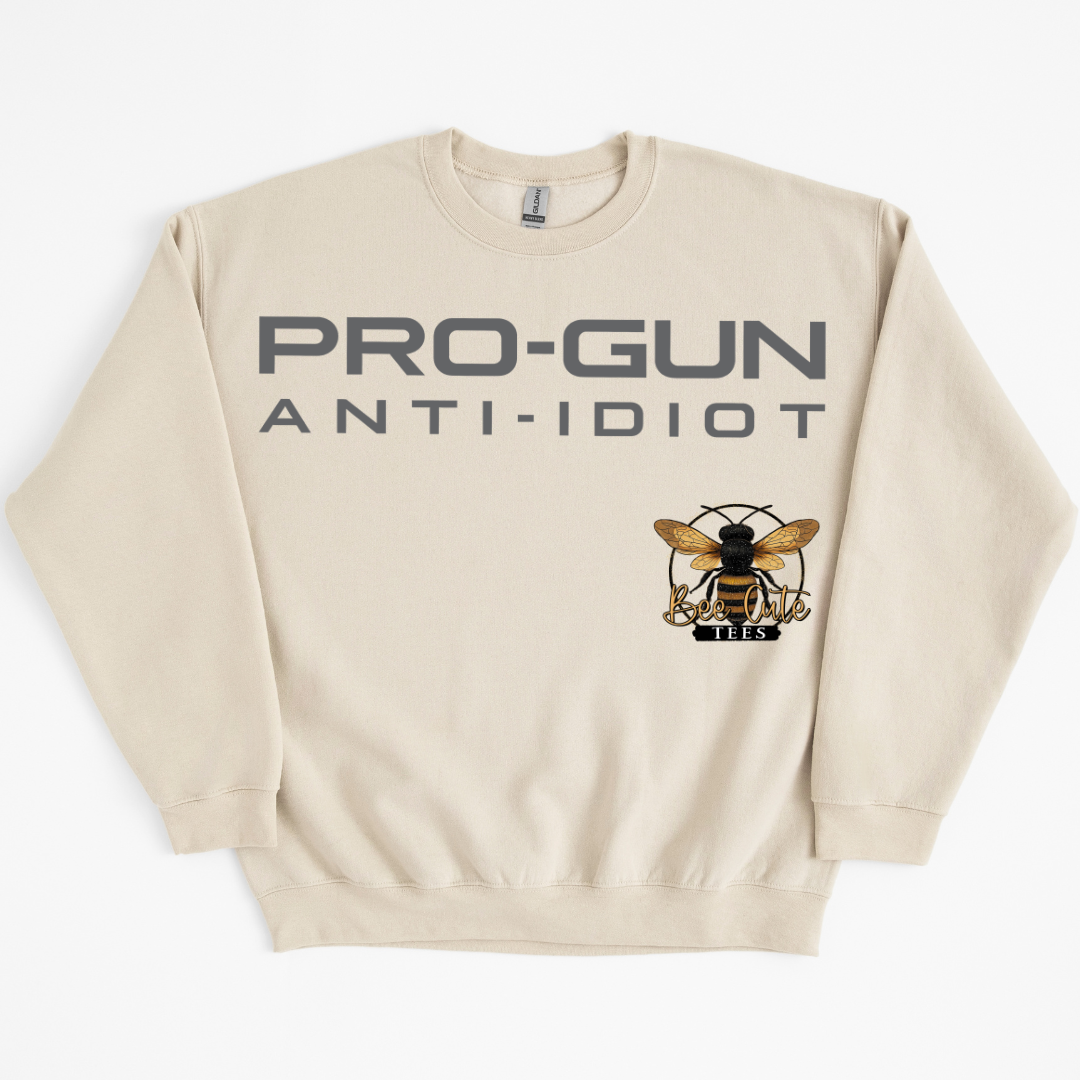 A cream-colored crewneck sweatshirt with 'PRO-GUN ANTI-IDIOT' printed in dark gray across the chest, and a graphic of a bee logo.