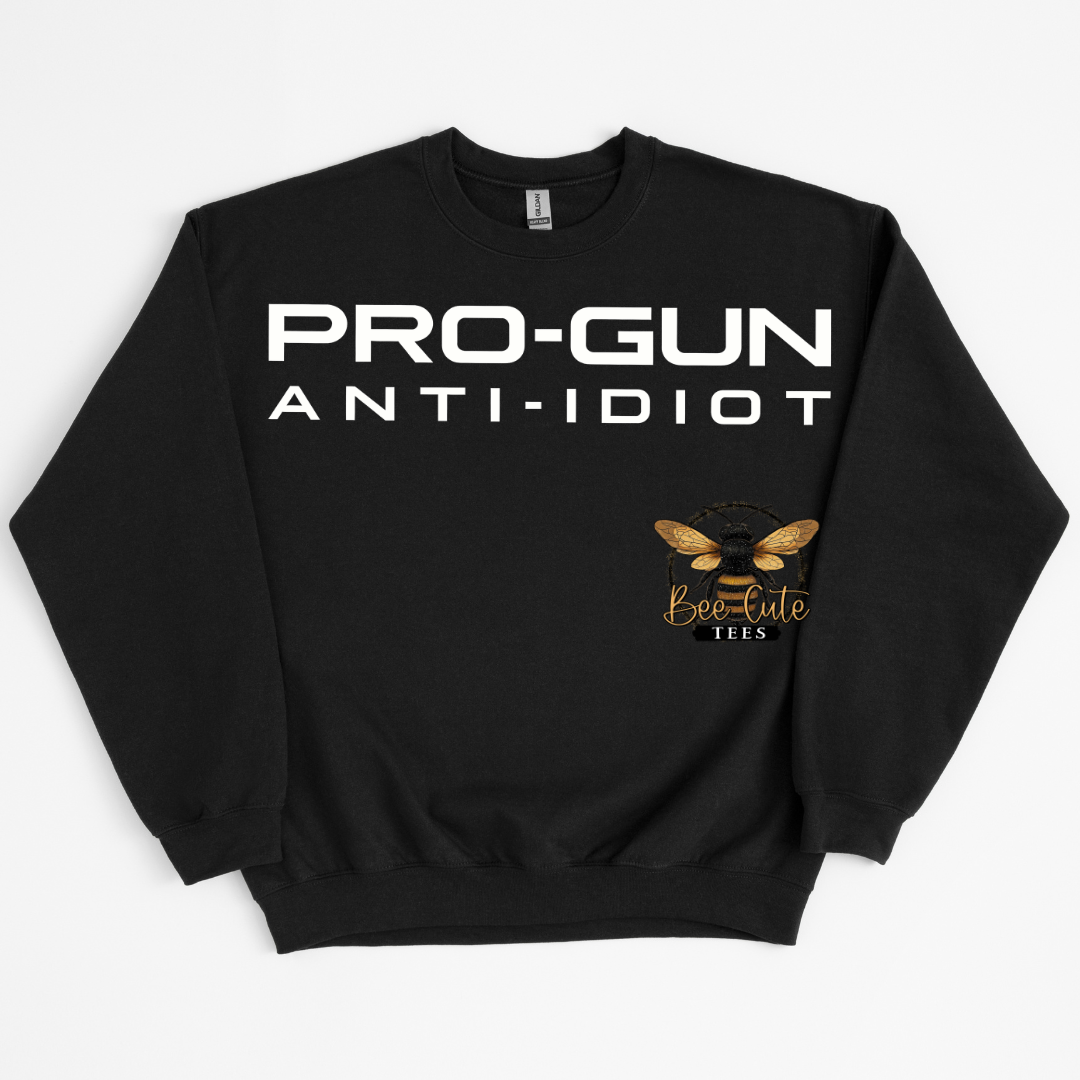 A black crewneck sweatshirt with 'PRO-GUN ANTI-IDIOT' printed in bold white letters across the chest, and a gold bee logo with 'Bee-Cute Tees' written below on the right side of the chest, displayed on a light gray background.
