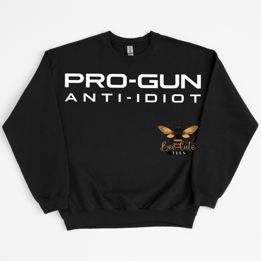A black crewneck sweatshirt with 'PRO-GUN ANTI-IDIOT' printed in bold white letters across the chest, and a gold bee logo with 'Bee-Cute Tees' written below on the right side of the chest, displayed on a light gray background.