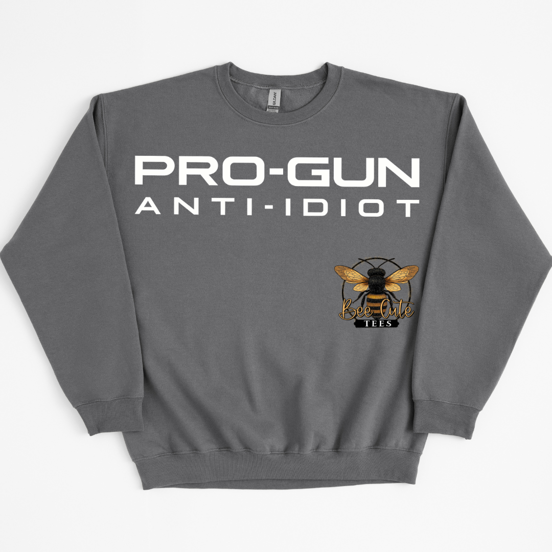 A dark gray crewneck sweatshirt with 'PRO-GUN ANTI-IDIOT' printed in bold white letters across the chest, and a logo of a bee with wings on the lower right side of the text.
