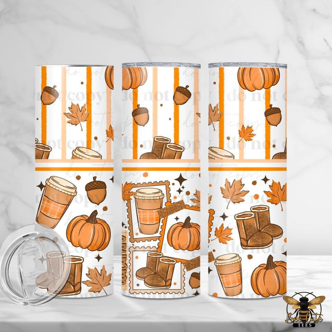 Three tall insulated tumblers with a fall-themed print featuring pumpkins, acorns, maple leaves, coffee cups, boots, and stars on a white background with orange stripes. A clear lid is shown in front on a light marble surface.