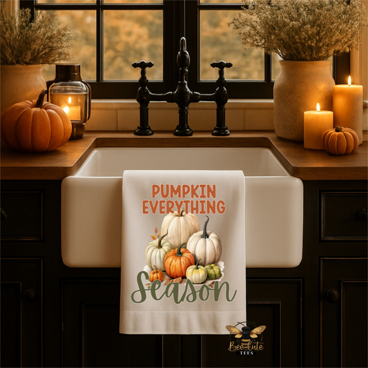 A white kitchen towel with a fall harvest design hanging over a farmhouse sink. The towel features the text 'PUMPKIN EVERYTHING Season' in orange and green lettering, surrounding an illustration of various pumpkins and gourds.