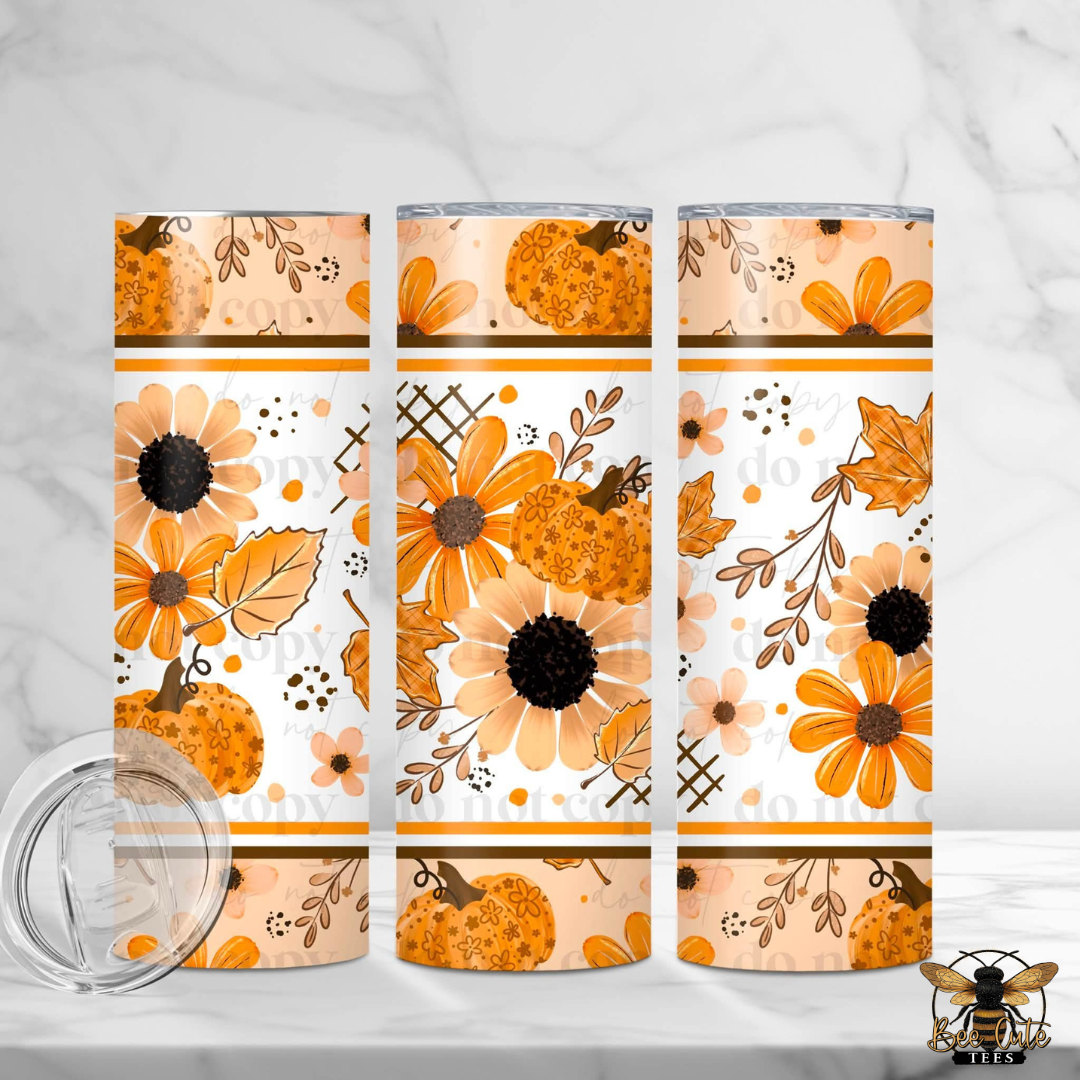Three insulated tumblers with a fall floral pumpkin pattern, shown on a white marble surface with a clear lid in the foreground. The pattern features orange pumpkins, orange flowers, and brown leaves on a white background.