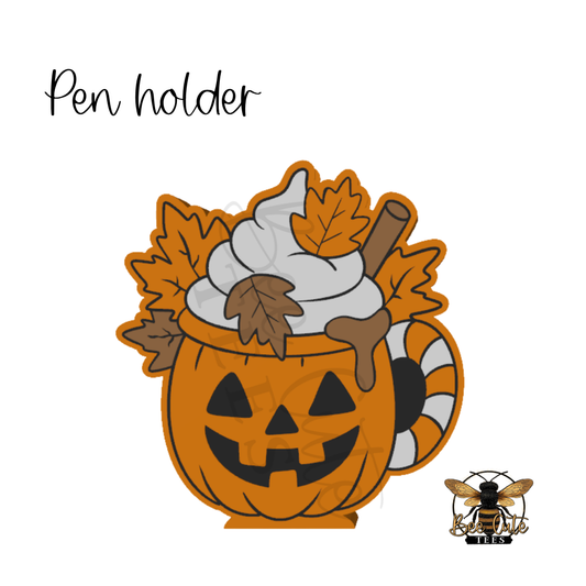 A Halloween-themed pumpkin mug pen holder featuring a jack-o'-lantern mug filled with whipped cream, autumn leaves, and a cinnamon stick, shown on a white background with the text 'Pen holder' and a small bee logo in the bottom right.