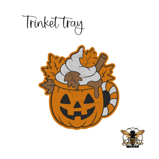 A Halloween-themed 'Trinket tray' design featuring a jack-o'-lantern mug filled with whipped cream, autumn leaves, and a cinnamon stick, shown on a white background with a bee logo in the bottom right.
