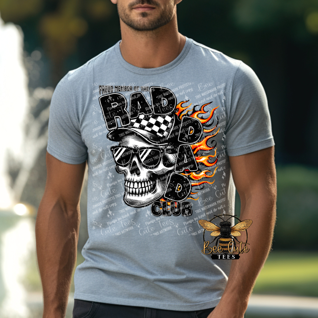 Man wearing a grey graphic tee featuring a skull in sunglasses and a checkered cap with flames in the background and the phrase “Proud Member of the Rad Dad Club” in bold distressed lettering.
