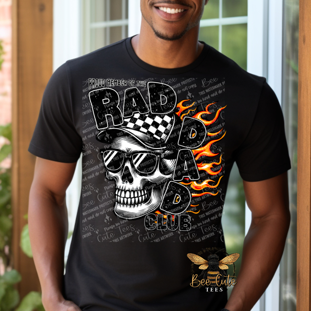 Man wearing a black graphic tee featuring a skull in sunglasses and a checkered cap with flames in the background and the phrase “Proud Member of the Rad Dad Club” in bold distressed lettering.
