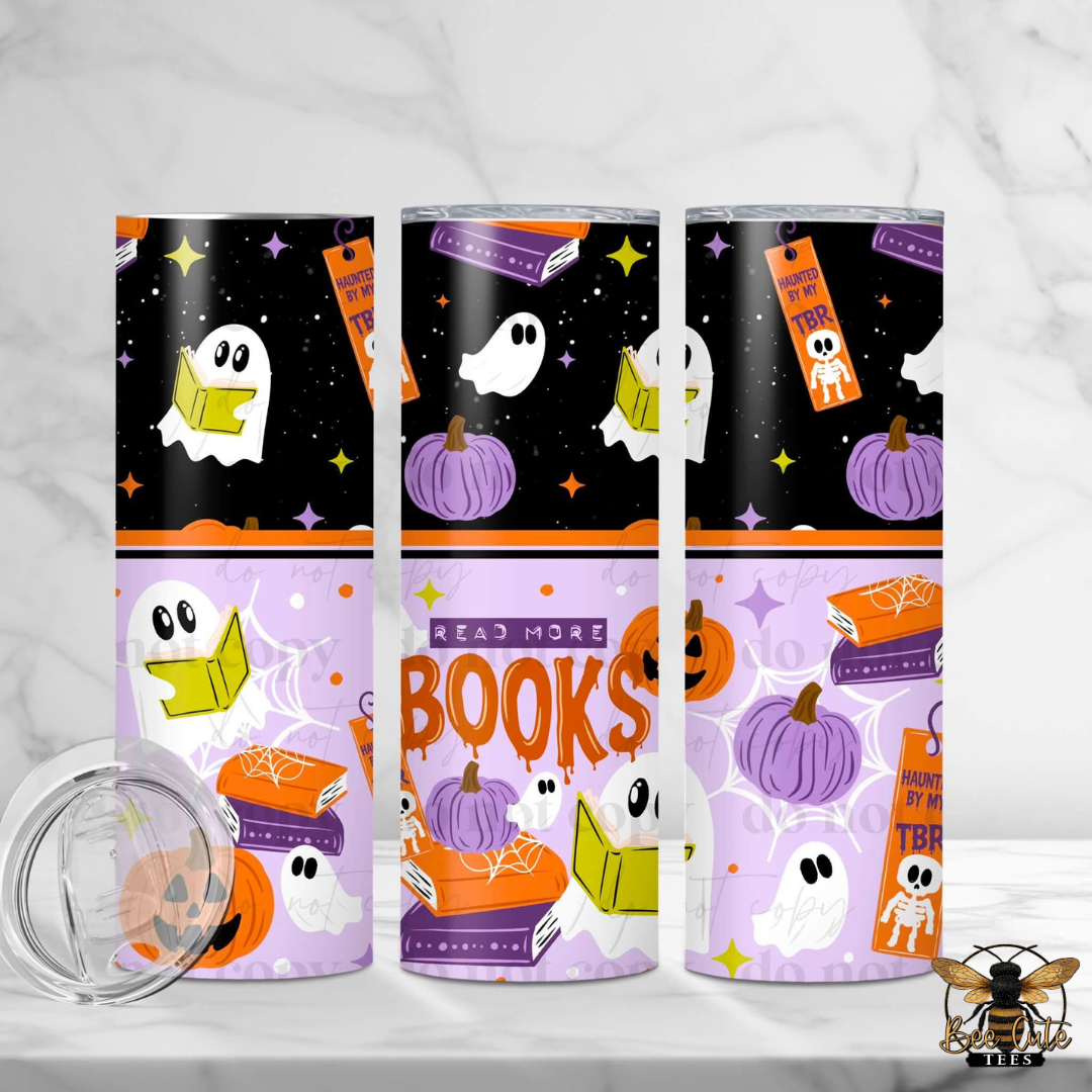 Three tall insulated tumblers with Halloween-themed wraparound prints are displayed on a light marble surface. The designs feature black, orange, purple, and white illustrations including ghosts reading books, pumpkins, stars, and the words 'READ MORE BOOKS' and 'Halloween TBR'.