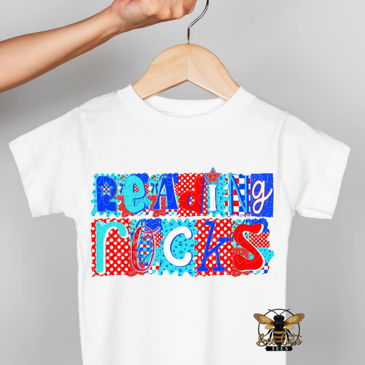 White t-shirt with colorful text 'READING ROCKS' on a hanger against a gray background