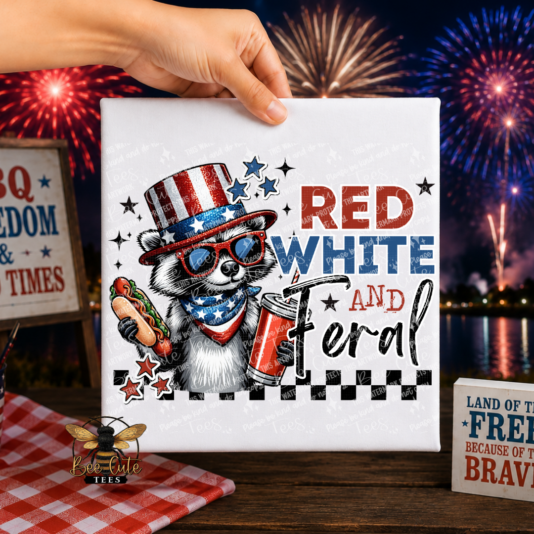 White t-shirt with a raccoon wearing an American flag hat and sunglasses, holding a hot dog and beer, with 'Red White and Feral' text, against a fireworks display background.
