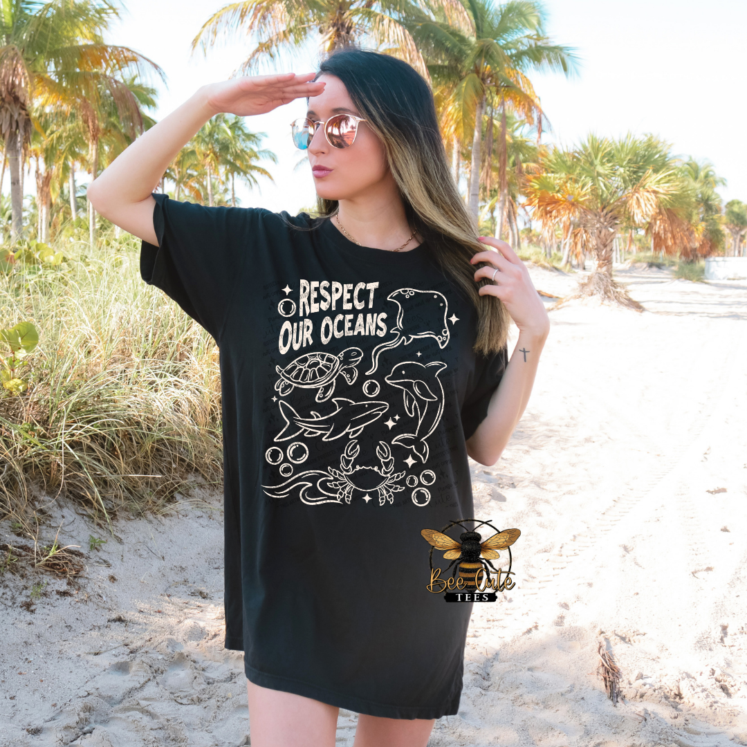 Woman wearing a black t-shirt with 'Respect Our Oceans' design on a beach.