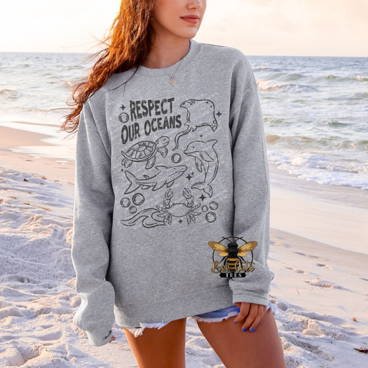 Person wearing a gray sweatshirt with ocean-themed design on a beach