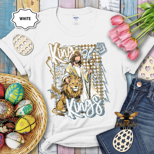 White t-shirt with 'King of Kings' design featuring a lion, surrounded by Easter eggs and flowers on a wooden surface.
