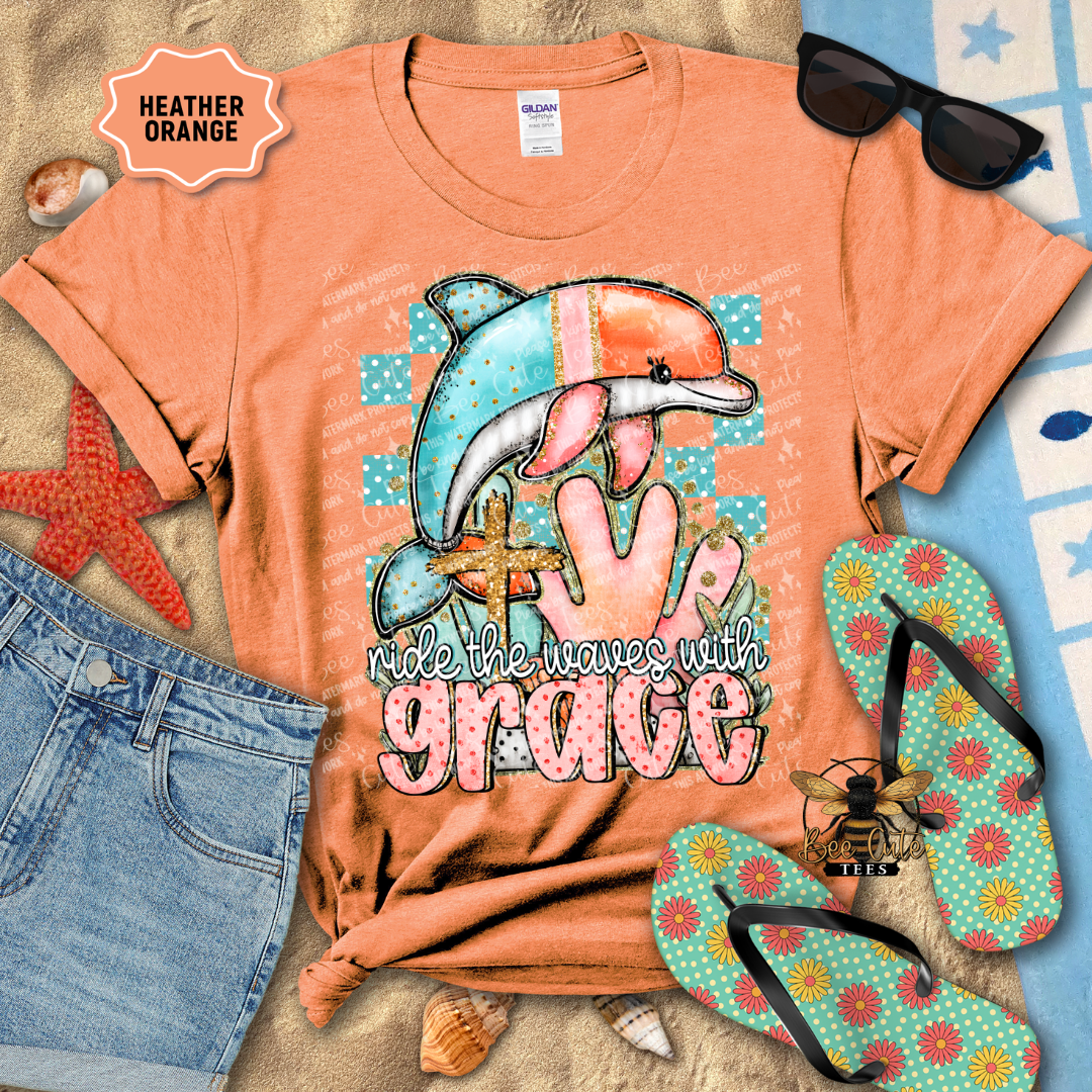 Orange t-shirt with dolphin graphic and text, surrounded by beach accessories on a textured surface.