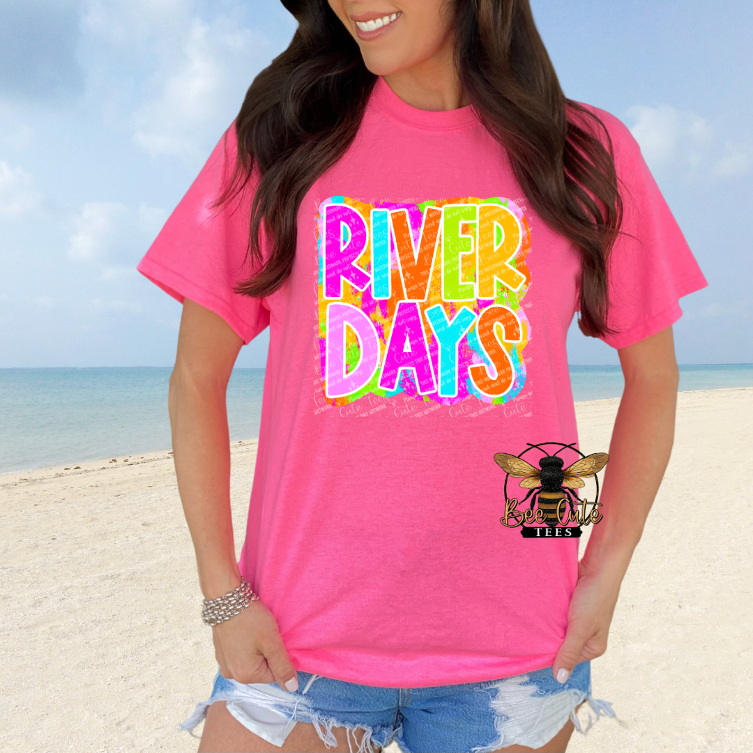 Person wearing a pink 'River Days' t-shirt on a beach