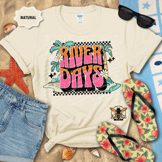 Beige t-shirt with 'River Days' graphic design, sunglasses, flip-flops, and beach accessories on a natural background.