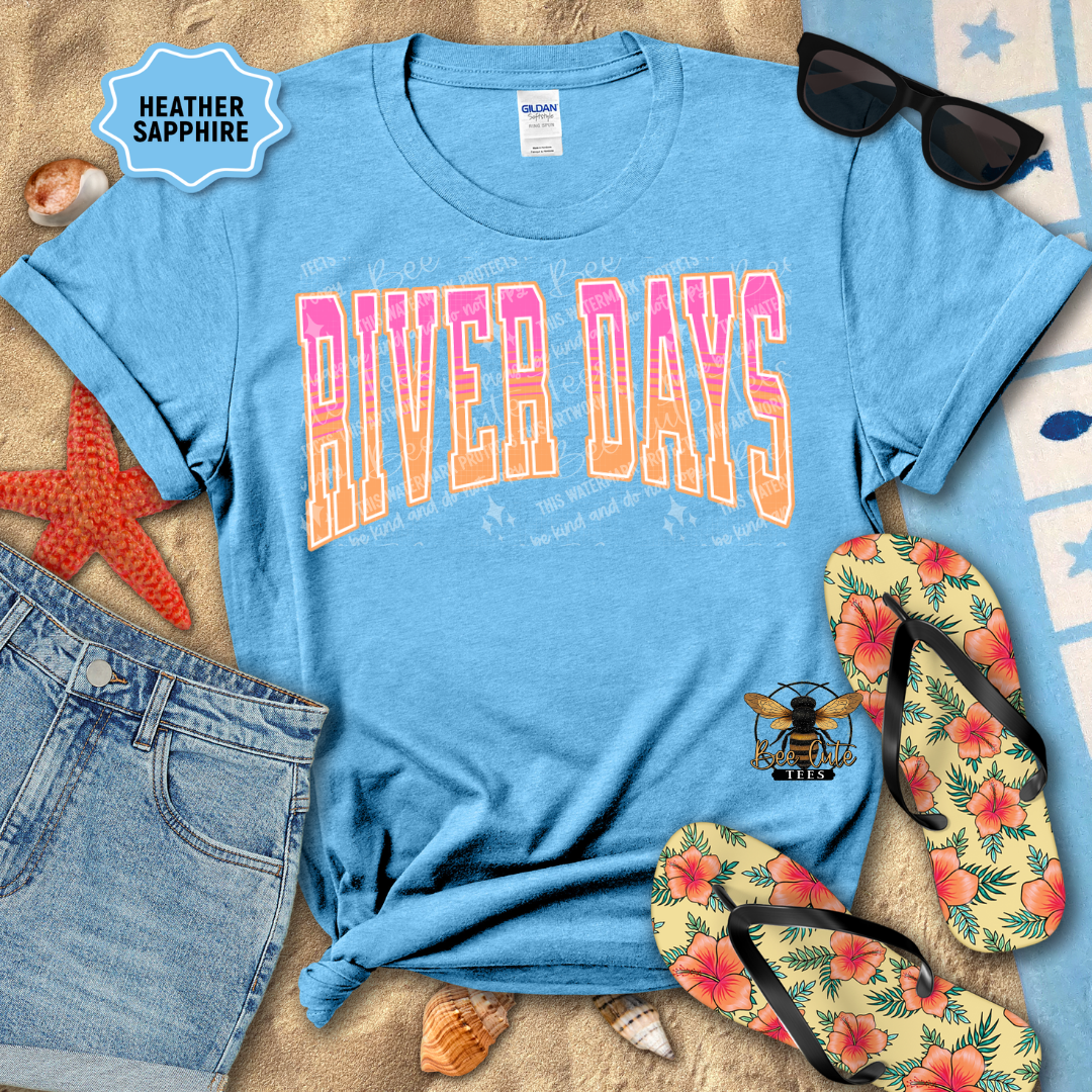 Blue t-shirt with 'River Days' design on sand with beach accessories