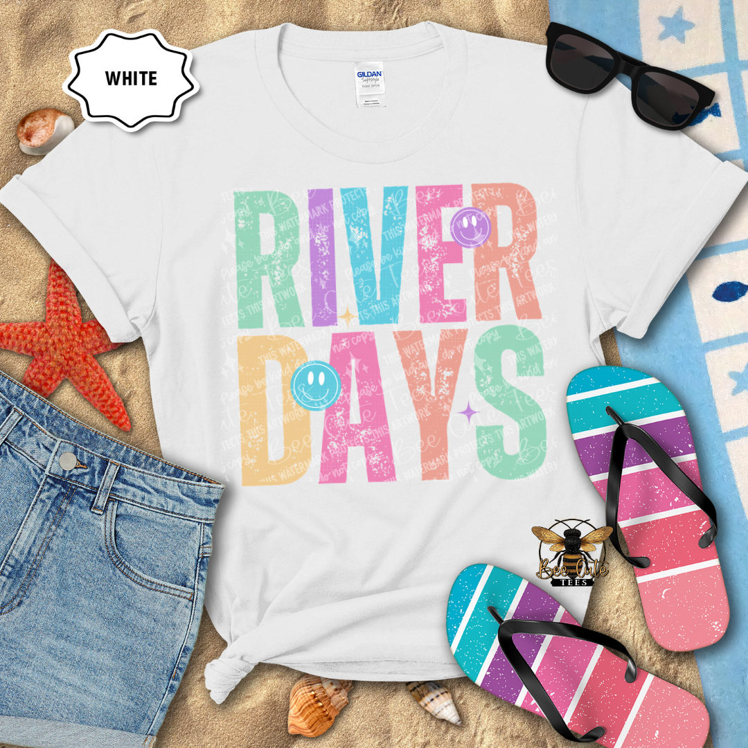White t-shirt with 'River Days' text, sunglasses, flip-flops, and beach accessories on a sandy background.