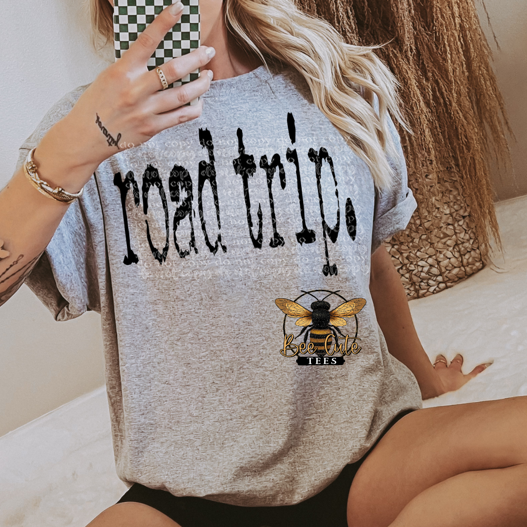 Person wearing a gray t-shirt with 'road trip.' and a bee logo design.
