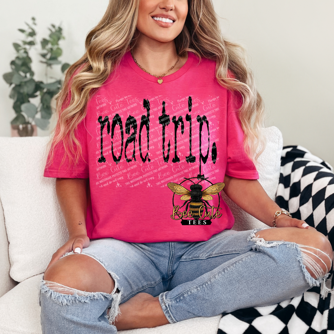 Person wearing a pink 'road trip' t-shirt with a graphic design, sitting on a couch.