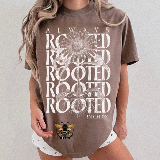 A woman wearing a brown oversized graphic t-shirt with 'ROOTED IN CHRIST' and a daisy design in white, paired with white shorts.