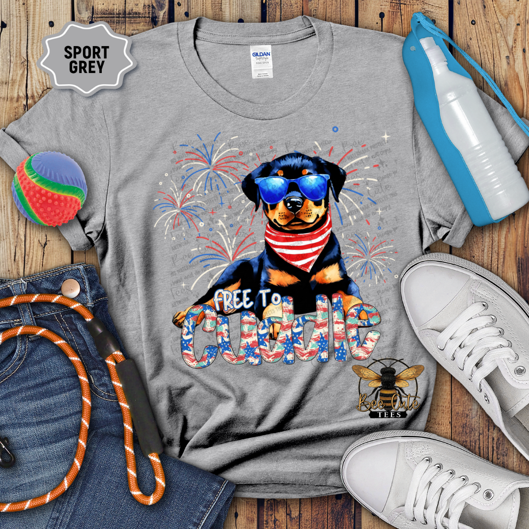 Gray t-shirt with a dog graphic and text, surrounded by jeans, shoes, and sports equipment on a wooden surface.