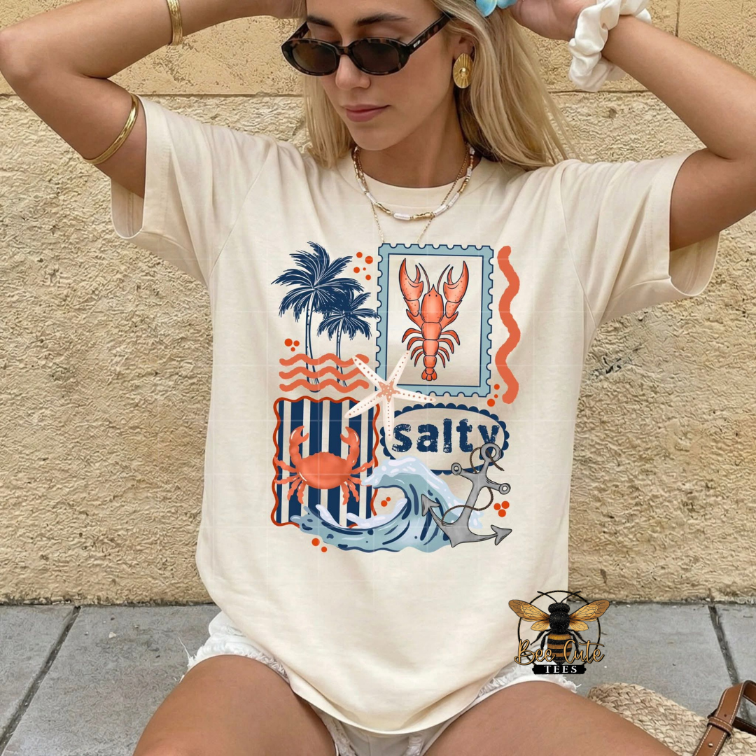 Woman wearing a t-shirt with a beach-themed graphic design against a stone wall.
