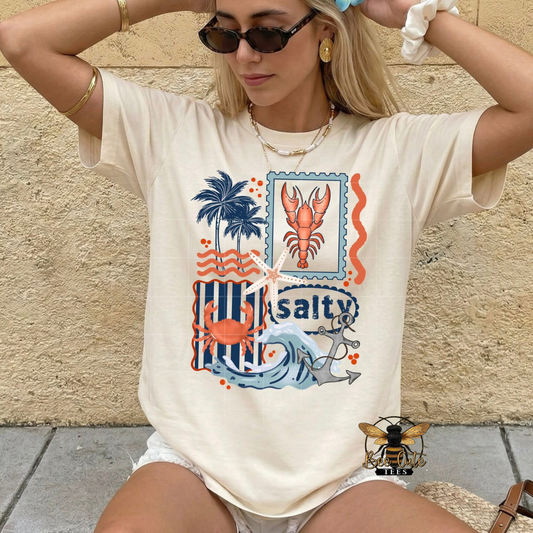 Woman wearing a t-shirt with a beach-themed graphic design against a stone wall.