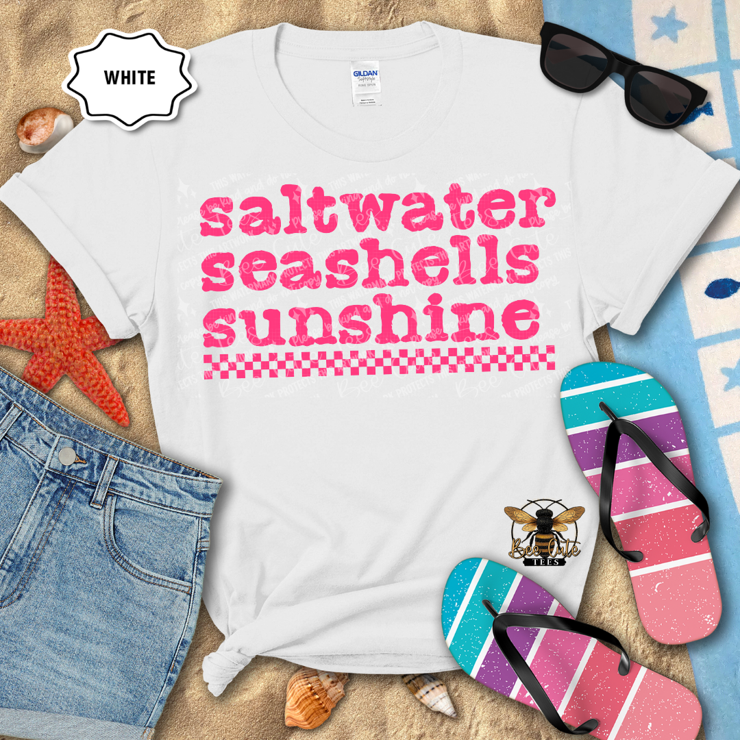 White t-shirt with 'saltwater seashells sunshine' text, sunglasses, flip-flops, and beach items on sand.