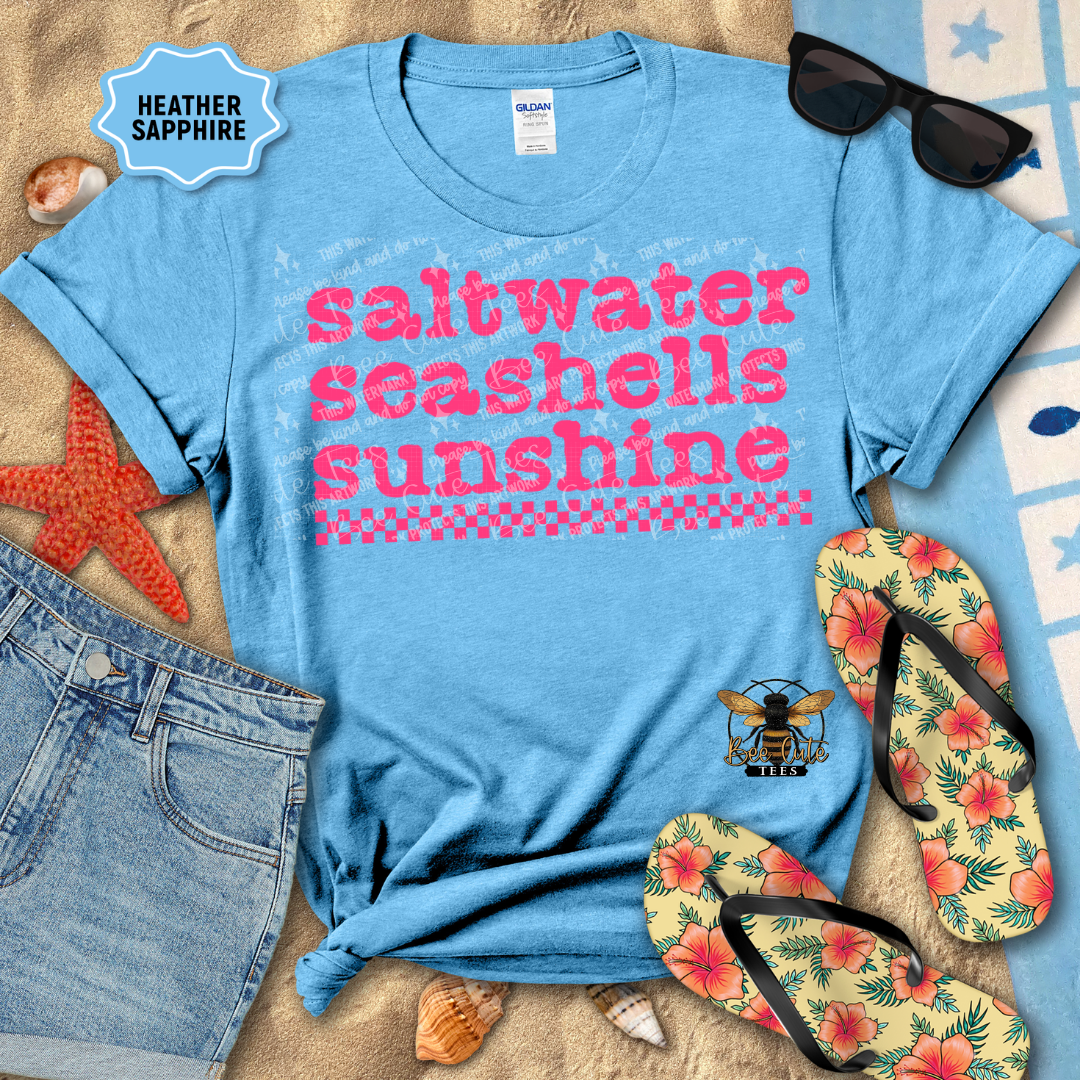 Blue t-shirt with 'saltwater seashells sunshine' text, sunglasses, flip-flops, and beach items on sand.
