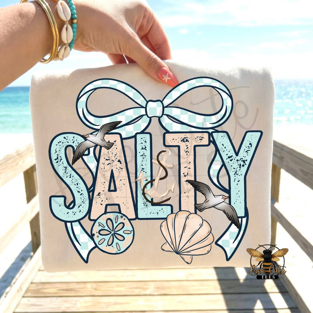 Beige t-shirt with 'Salty' design featuring a bow, seagulls, and a shell on a beach background.