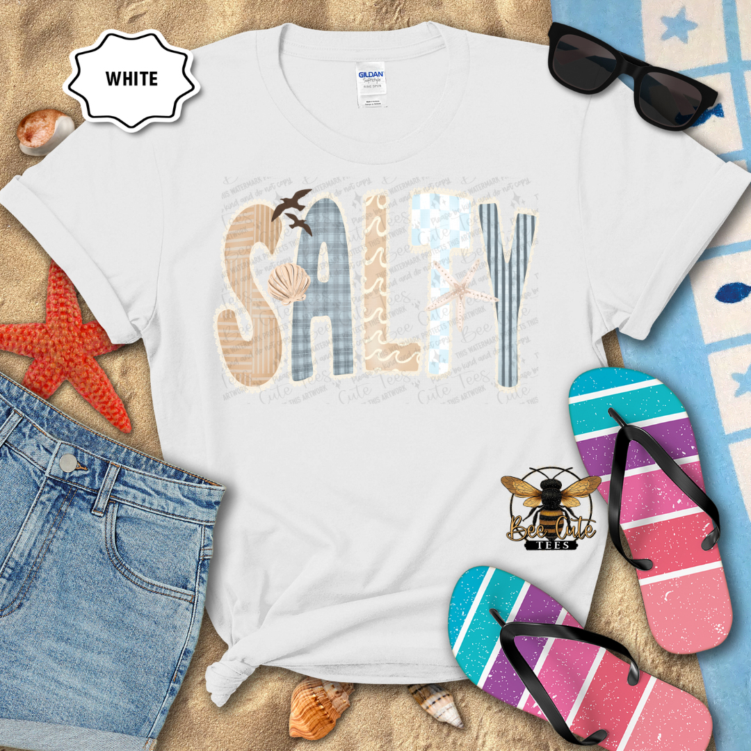 White t-shirt with 'SALTY' design, sunglasses, and flip-flops on a beach-themed background