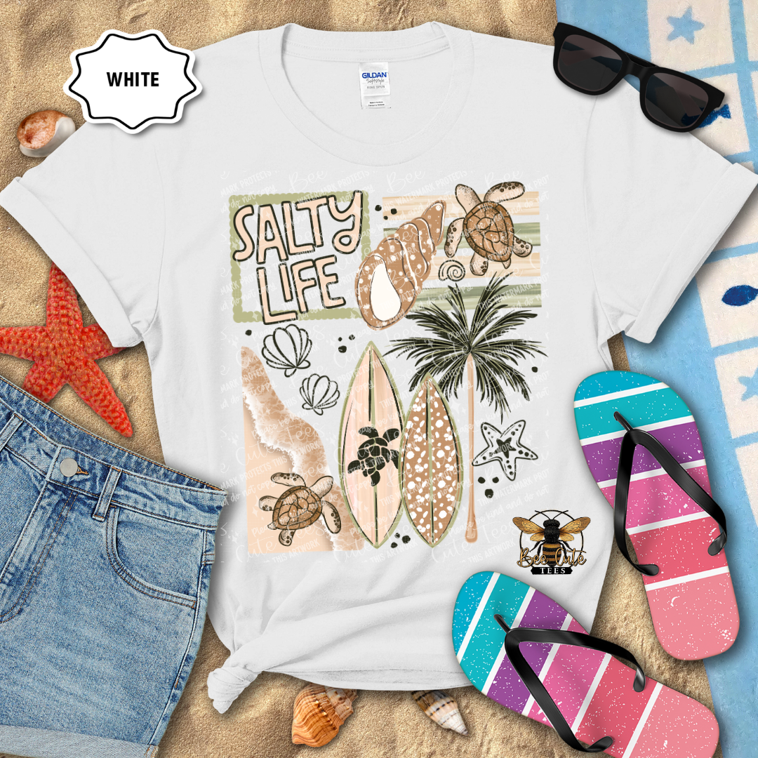 White t-shirt with 'Salty Life' design featuring surfboards, turtles, and palm trees on a beach-themed background.