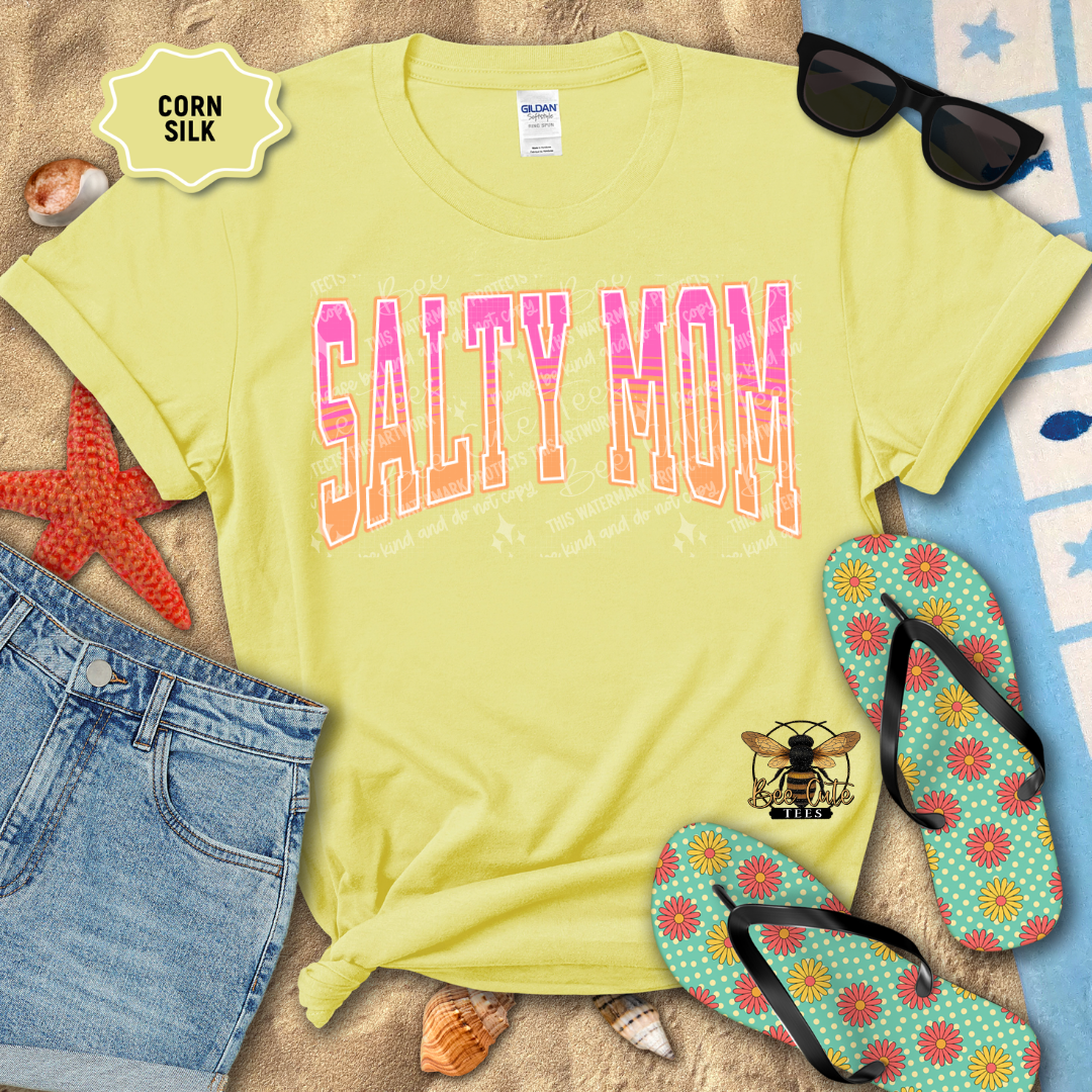 Yellow t-shirt with 'Salty Mom' text, sunglasses, denim shorts, and flip-flops on a beach-themed background.