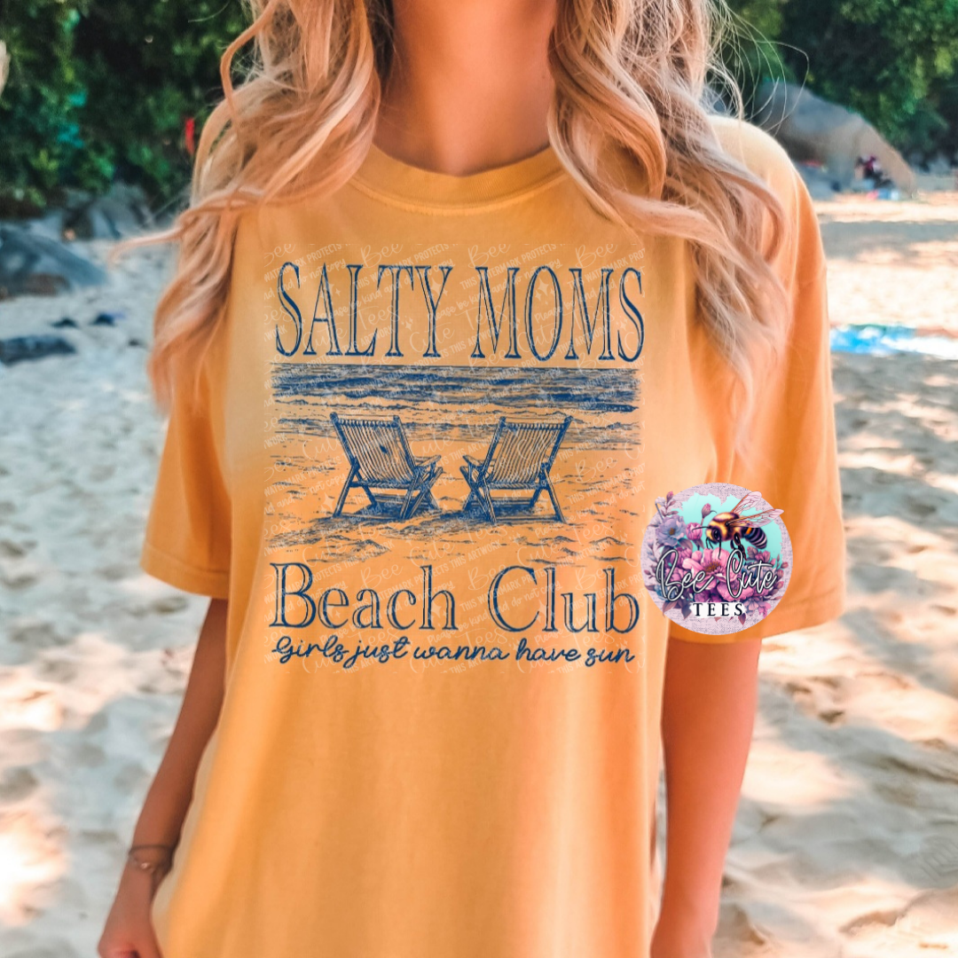 Person wearing a yellow 'Salty Moms Beach Club' t-shirt on a beach.