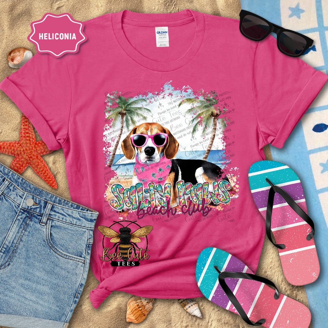 Pink t-shirt with a dog graphic and 'Beach Club' text, surrounded by beach accessories.
