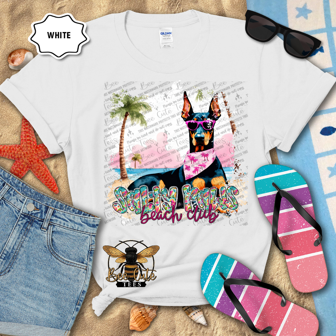 White t-shirt with a dog graphic and 'Salty Paws Beach Club' text, surrounded by beach accessories.