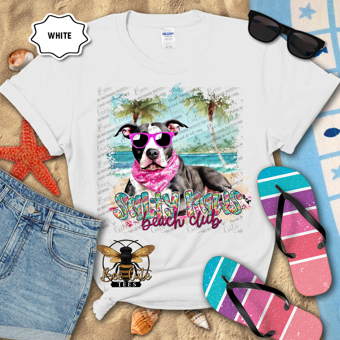 White t-shirt with a dog graphic and 'Beach Club' text, surrounded by beach accessories.