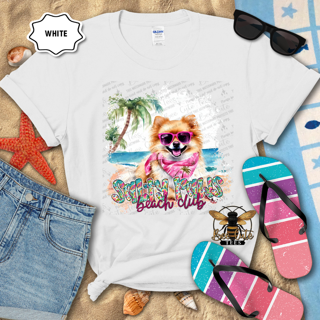 White t-shirt with a dog graphic and 'Beach Club' text, surrounded by beach accessories.