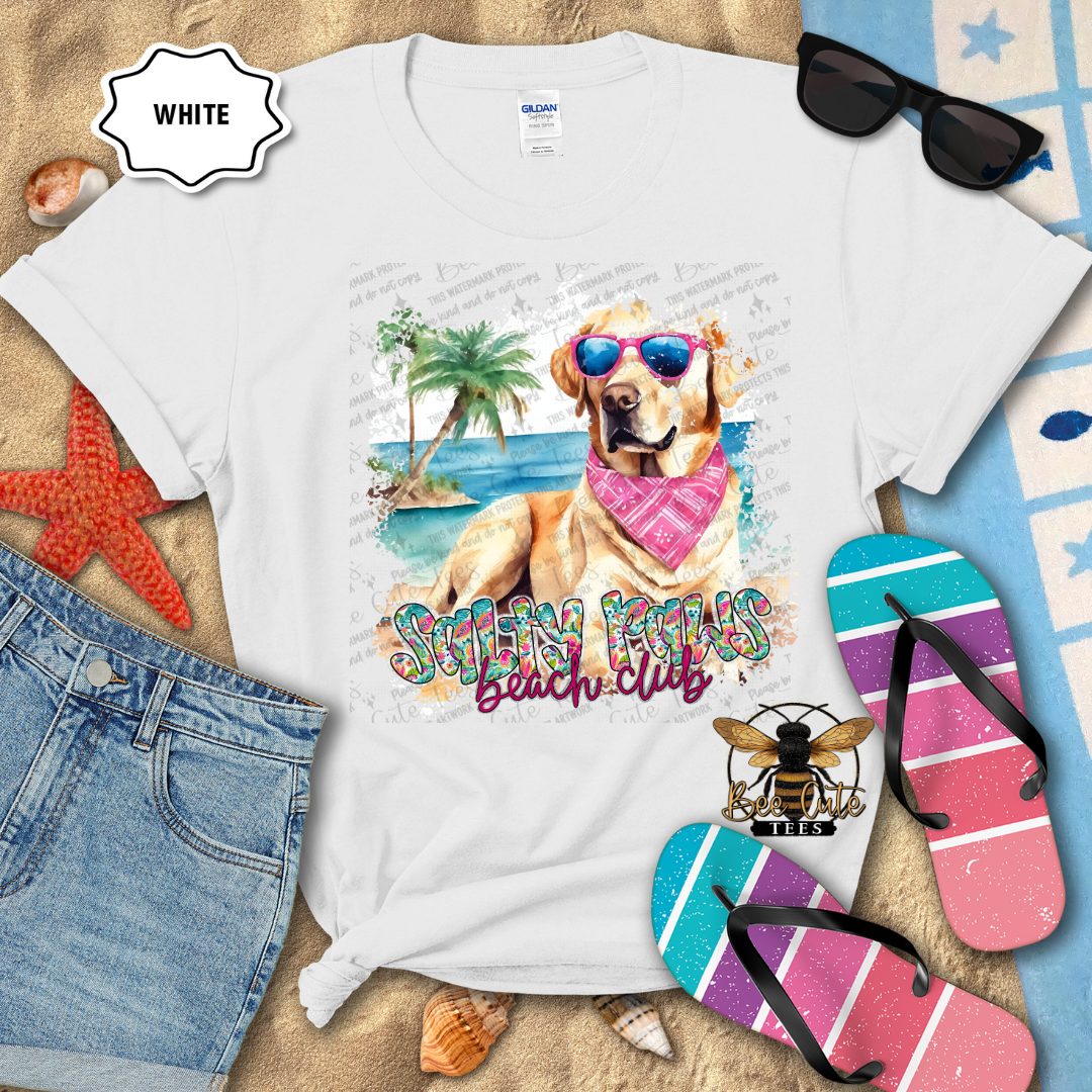 White t-shirt with a beach-themed design featuring a dog, sunglasses, and flip-flops on a sandy background.