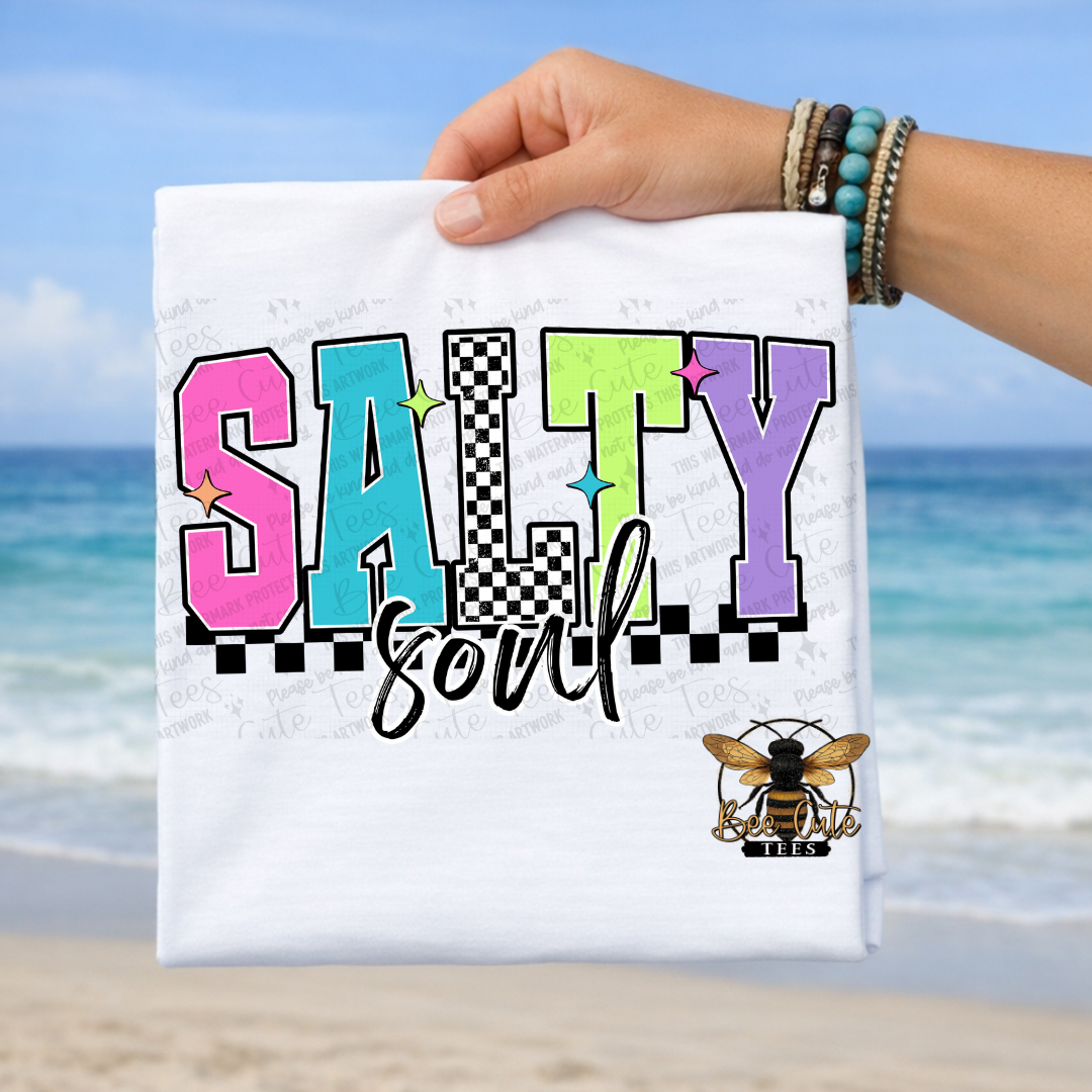 Towel with 'Salty Soul' text and bee logo held by a hand on a beach.