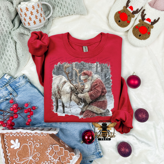 Red sweatshirt with Santa and reindeer design, surrounded by Christmas decor on a white surface.